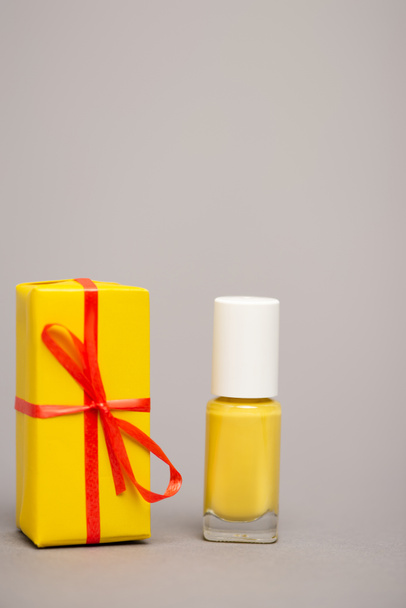 wrapped yellow gift box near bottle with nail polish isolated on grey - Фото, изображение
