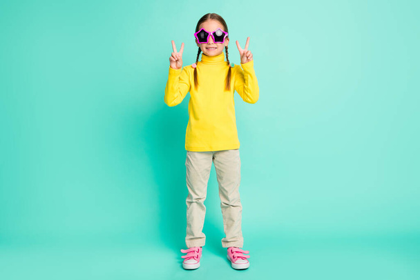 Full size of pretty girl make two v-sing wear yellow turtleneck white pants star sunglass isolated on shine teal color background - Фото, зображення