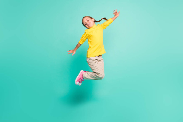 Full size photo of happy girl jump in air wear yellow turtleneck white pants isolated on shine teal color background - Фото, изображение