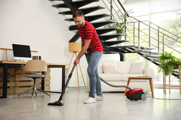 Young man using vacuum cleaner in living room - Foto, imagen