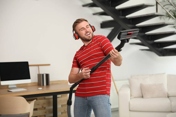 Young man having fun while vacuuming in living room - Foto, afbeelding