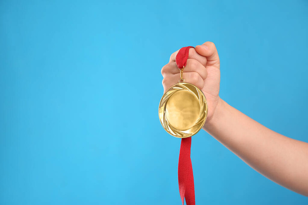 Woman holding gold medal on light blue background, closeup. Space for text - Photo, Image