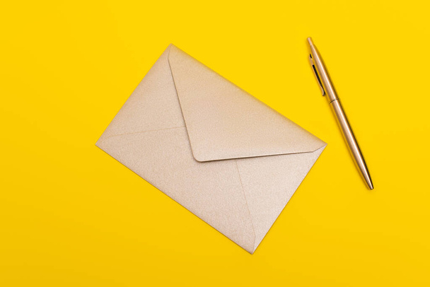 верхний вид конверта рядом с золотой ручкой изолирован на желтый - Фото, изображение
