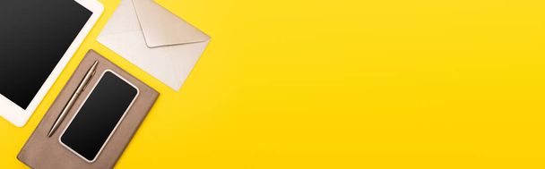 верхний вид устройств с чистым экраном рядом с ноутбуком с золотой ручкой рядом конверт изолирован на желтый, баннер - Фото, изображение