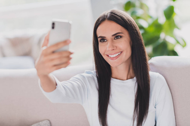 Photo of positive pretty young woman hold phone take selfie nice smile sit couch indoors inside house - Fotó, kép