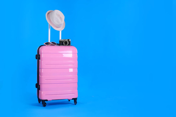 Travel suitcase with hat, camera and sunglasses on light blue background, space for text. Summer vacation - Foto, immagini