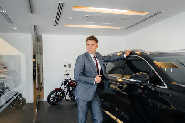 Un joven hombre de negocios mira un coche nuevo en un concesionario de automóviles. Comprar un coche - Foto, imagen