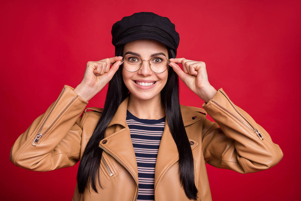 Portrait of charming person hands touching eyewear smile black headwear isolated on red color background - Φωτογραφία, εικόνα