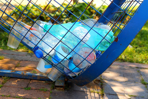  Plastikmüll, Flaschen in der Urne von Metallstangen auf dem Gehweg und Gras in Großaufnahme. - Foto, Bild