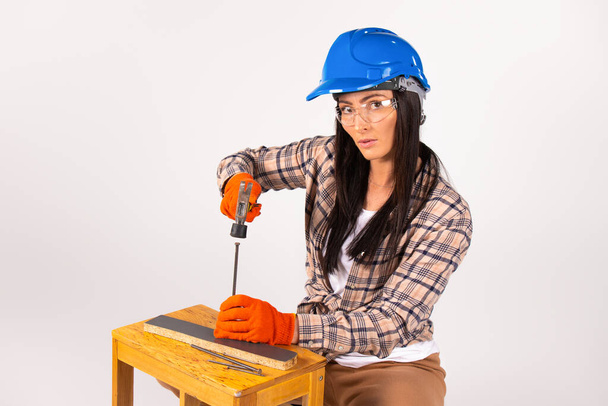 Serious independent woman in a helmet and glasses with a hammer looks at the camera on a white background. - Фото, зображення