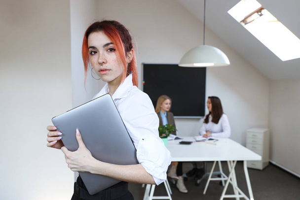 Porträt einer Geschäftsfrau mit Laptop vor dem Hintergrund eines arbeitenden Büros - Foto, Bild
