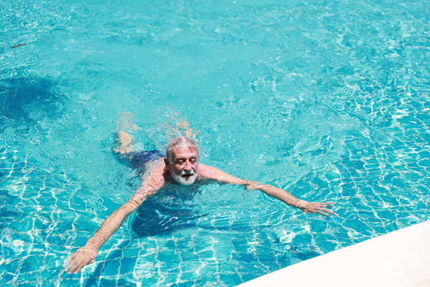 heureux vieux caucasien homme nager dans la piscine pendant les vacances de retraite avec détente et sourire - Photo, image