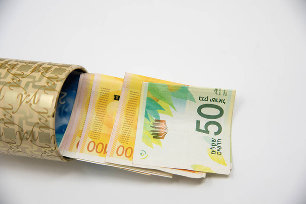 Металлическая копилка с символикой нового Израиля Шекеля для экономии денег. На белом фоне с банкнотами NIS  - Фото, изображение