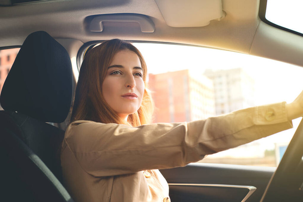 Egy figyelmes, csinos fiatal nő portréja, aki autót vezet egy napsütéses napon.. - Fotó, kép