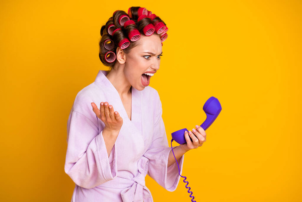 Profile side view portrait of pretty evil mad fury woman wearing curlers talking on phone yelling isolated bright yellow color background - Photo, image