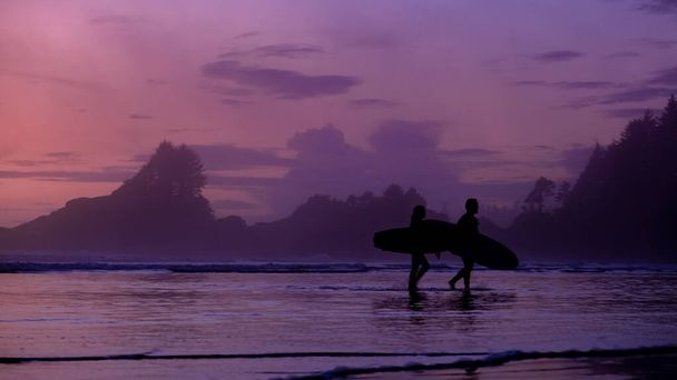 Tofino Vancouver Island Pacifische kust, surfers met boord bij zonsondergang op het strand, surfers silhouet Canada Vancouver Island Tofino.  - Foto, afbeelding