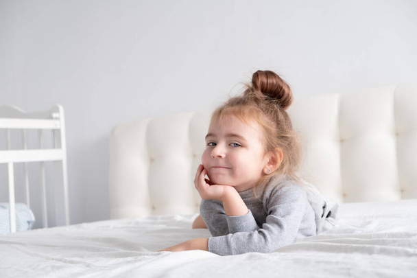 little girl in grey turtleneck having fun on white bedding. - Foto, immagini