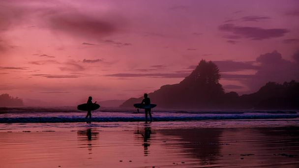 Tofino Vancouver Island Pacifische kust, surfers met boord bij zonsondergang op het strand, surfers silhouet Canada Vancouver Island Tofino.  - Foto, afbeelding