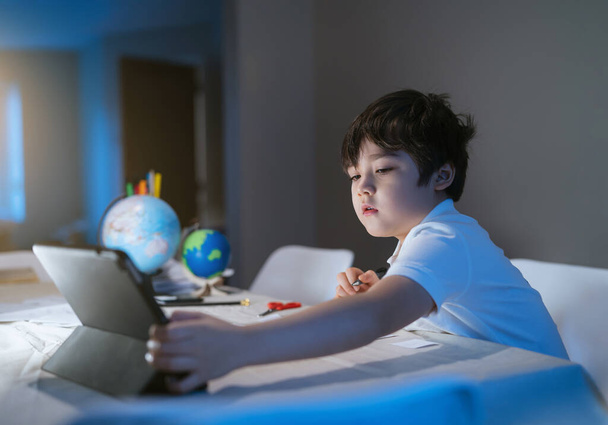 New normal life kid using tablet for his homework in cinematic tone, Child boy doing homework by using digital tablet searching information on internet,E-learning, Home schooling education concept - Photo, Image