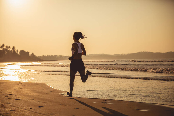 日の出のビーチを走る若いフィットネス女性  - 写真・画像