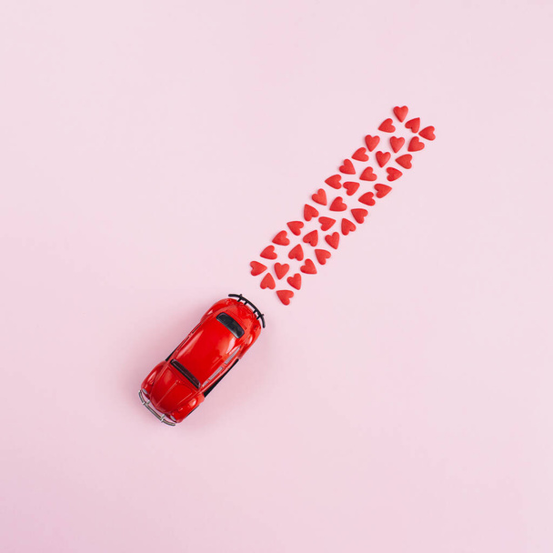 Sevgililer Günü geçmişi 14 Şubat. Kırmızı oyuncak araba, pembe arka planda kalp konfetisi. Sevgililer Günü yaratıcı konsepti. Teslimat. 8 Mart, Mutlu Kadınlar Günü. Düz konum, üst görünüm, kopyalama alanı - Fotoğraf, Görsel