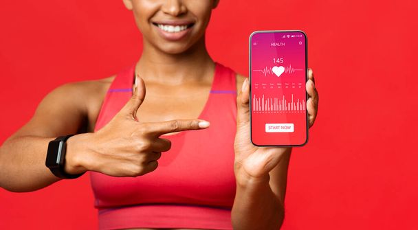 Mujer negra mostrando Smartphone con aplicación Cardio Tracker, fondo rojo - Foto, Imagen