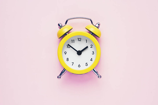 Reloj despertador vintage amarillo sobre fondo rosa. Concepto de ahorro de luz. Colocación plana, espacio de copia. - Foto, imagen