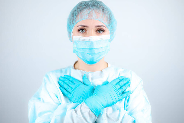 een verpleegster in een medisch gewaad, masker en beschermende handschoenen duwde haar handen tegen haar borst. - Foto, afbeelding