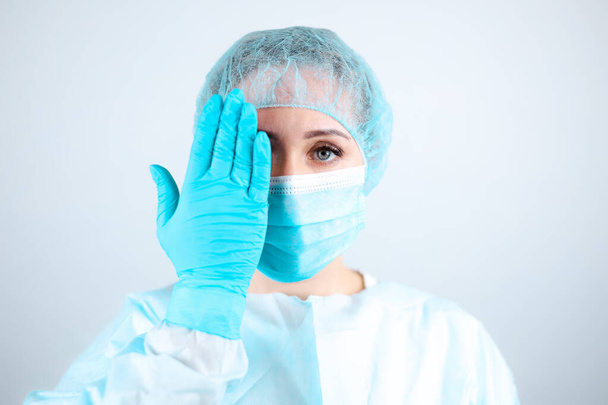 uma enfermeira com um vestido médico, máscara e luvas de proteção cobriu os olhos com as mãos - Foto, Imagem