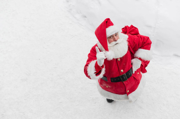 Top view on friendly santa claus actively gesturing and wishing merry christmas. An elderly man in a Santa costume stands on the snow outside and wishes a happy new year. - Photo, image
