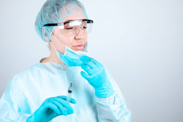 Egy nővér orvosi köpenyben, maszkban és védőkesztyűben, átlátszó szemüveggel az arcán leveszi a maszkot, hogy levegőt lélegezzen. - Fotó, kép