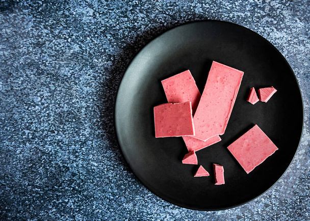 Vaaleanpunainen tai rubiinisuklaa, trendikäs jälkiruoka mustalla lautasella, kopiotila - Valokuva, kuva
