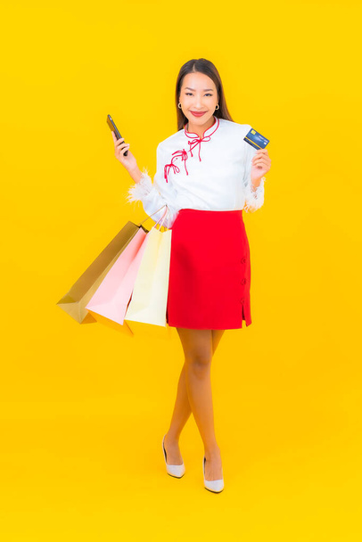 Retrato hermosa joven mujer asiática con bolsa de compras y tarjeta de crédito sobre fondo amarillo - Foto, imagen