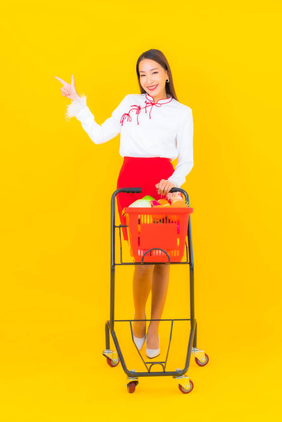 Porträt schöne junge asiatische Frau mit Einkaufskorb aus dem Supermarkt auf gelbem Hintergrund - Foto, Bild