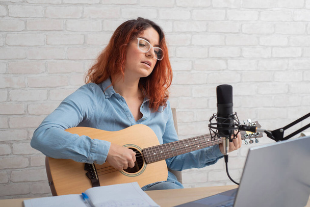 A woman sings into a microphone and plays the guitar live on a laptop. Girl musician recording a video blog - Zdjęcie, obraz
