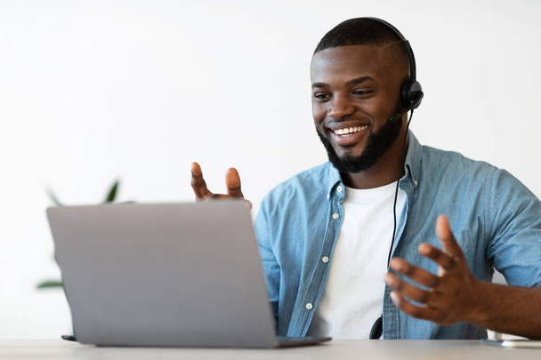 Videoconferencia. Alegre hombre afroamericano en auriculares haciendo llamada web en el ordenador portátil - Foto, Imagen