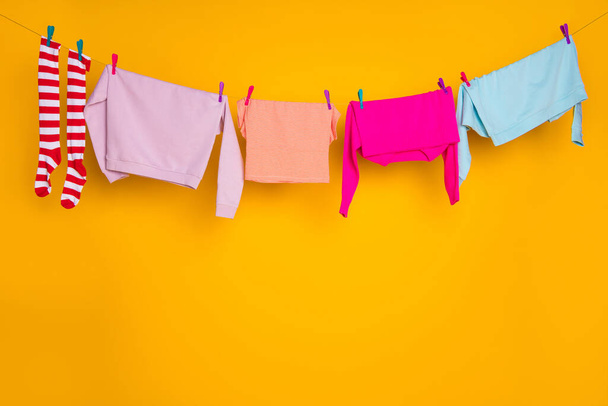 Colorful washed things wear garment hanging on rope hand eco cycle isolated over bright orange color background - 写真・画像