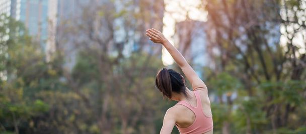 公園の屋外でピンクのスポーツウェアストレッチ筋肉を身に着けている若い大人の女性、スポーツ女性は朝のランニングやジョギングの準備ができて暖まる。ウェルネスフィットネス運動ワークライフバランスの概念 - 写真・画像