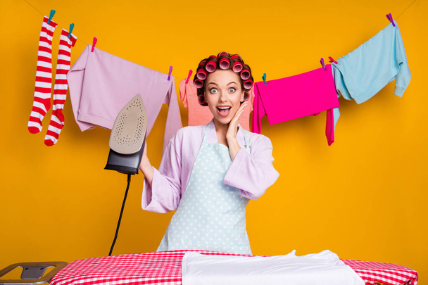Portrait of attractive amazed cheerful maid ironing fresh washed things isolated over bright orange color background - Foto, Bild