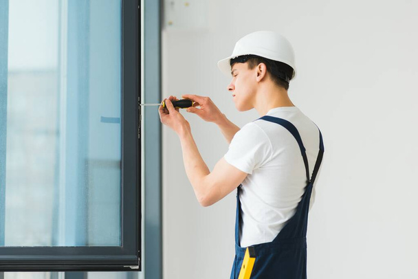 Workman in overalls installing or adjusting plastic windows in the living room at home - Φωτογραφία, εικόνα