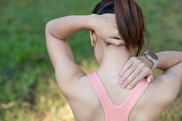 Молодая фитнес-женщина держит свою спортивную травму шеи, мышцы болеют во время тренировки. Азиатская бегунья, у которой проблемы с телом после тренировки летом - Фото, изображение