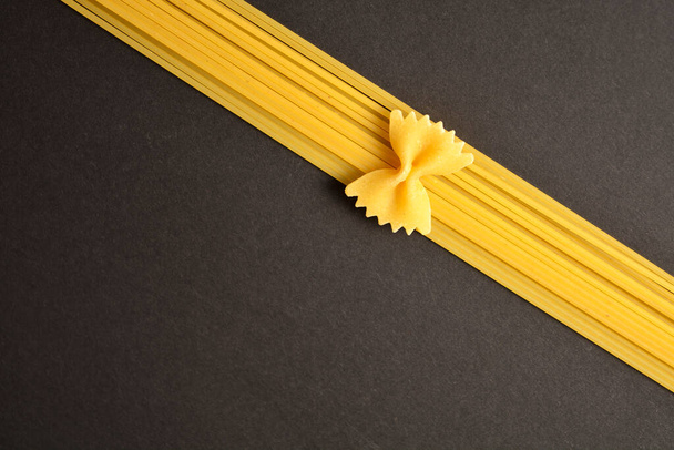 暗い背景に隔離されたスパゲティ上の生のイタリアのファーレ弓パスタ作品.リボンと弓の食品模倣 - 写真・画像