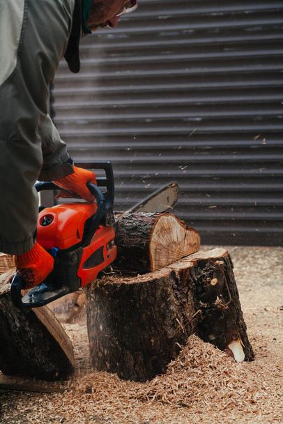 chainsaw is working. A man is sawing a piece of a tree trunk with a chainsaw. The piece stands on a large tree stump in the yard - Φωτογραφία, εικόνα