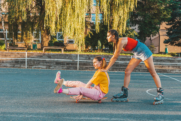 Two teen girls having fun with skate board. One girl pushes other from behind - Fotoğraf, Görsel