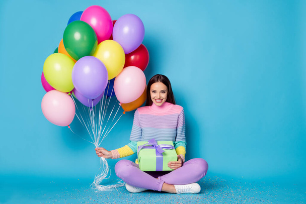 Full length photo of pretty girl sit floor legs crossed hold balloons gift box wear pullover isolated blue color background - 写真・画像