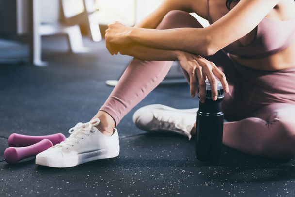 Sport woman workout at fitness center with relax and taking a break Beautiful girl holding protein shake bottle after exercise at gym Young lady get tired Healthy lifestyle Fitness and sport concept - Foto, afbeelding