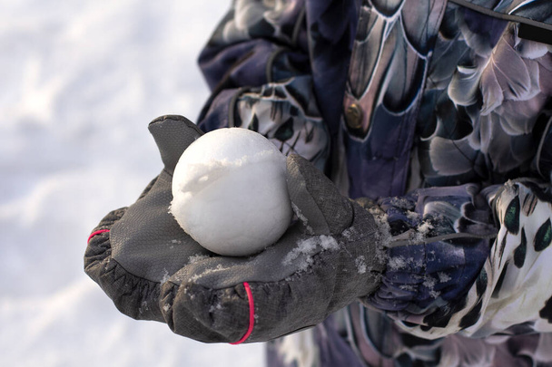 Bola de nieve en las manos de los niños con guantes impermeables. Primer plano. Primera nieve para juegos. Lanzar bolas de nieve en invierno. juegos activos en la nieve - Foto, imagen