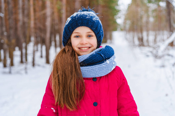 Portret małej szczęśliwej dziewczynki zimą w pokrytym śniegiem kapeluszu spacerującej po zimowym lesie - Zdjęcie, obraz