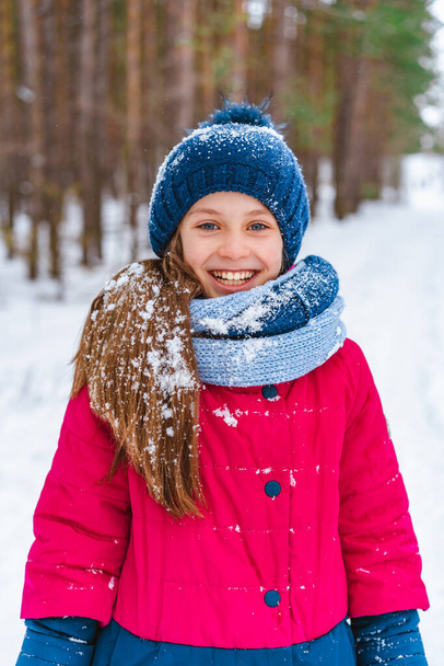Portrait of a little happy girl in winter in a snow-covered hat who walks in the winter forest - Φωτογραφία, εικόνα