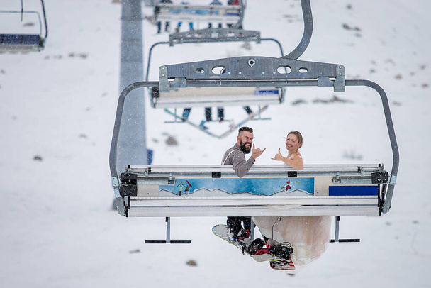 The bride and groom rising in the winter on a lift in a ski resort with snowboards - Photo, Image